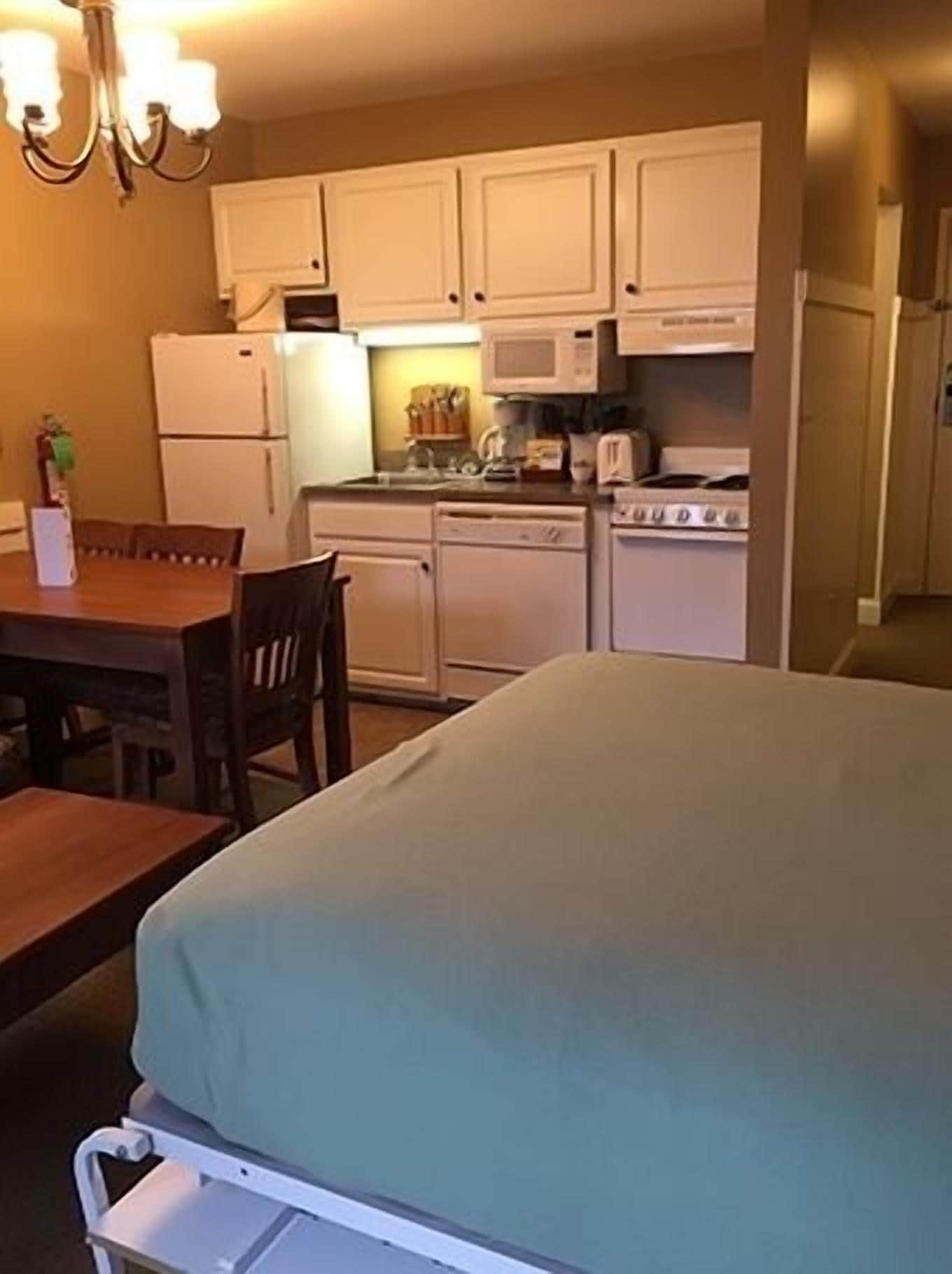 Una habitación de hotel compacta con cama, una pequeña mesa de comedor y servicios básicos de cocina, incluyendo microondas, estufa y refrigerador.