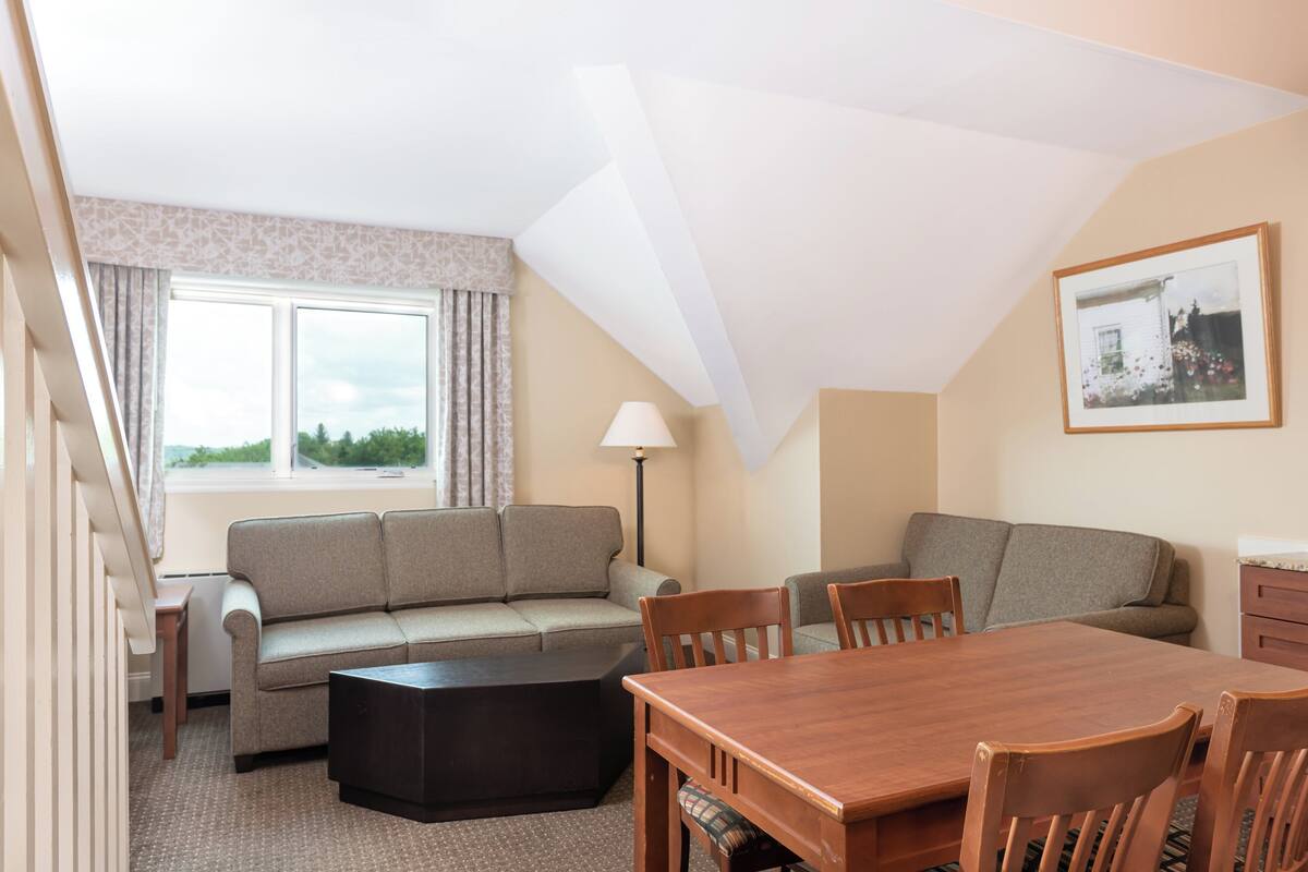 A cozy room with a sofa, a dining table, and chairs. There is a lamp and a window with curtains.