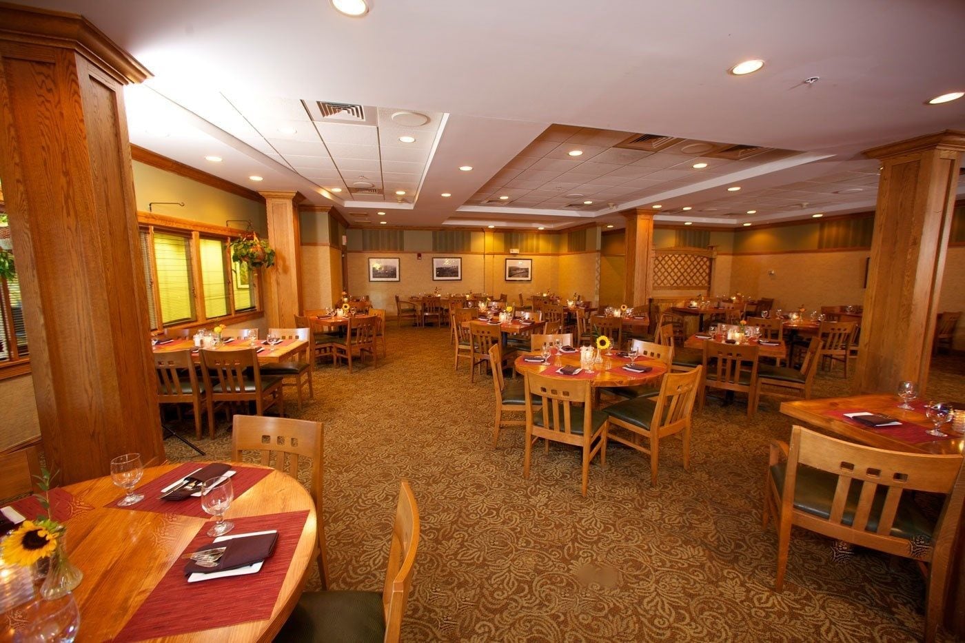 A spacious dining area with multiple tables and chairs, wooden paneling, and a patterned carpet.