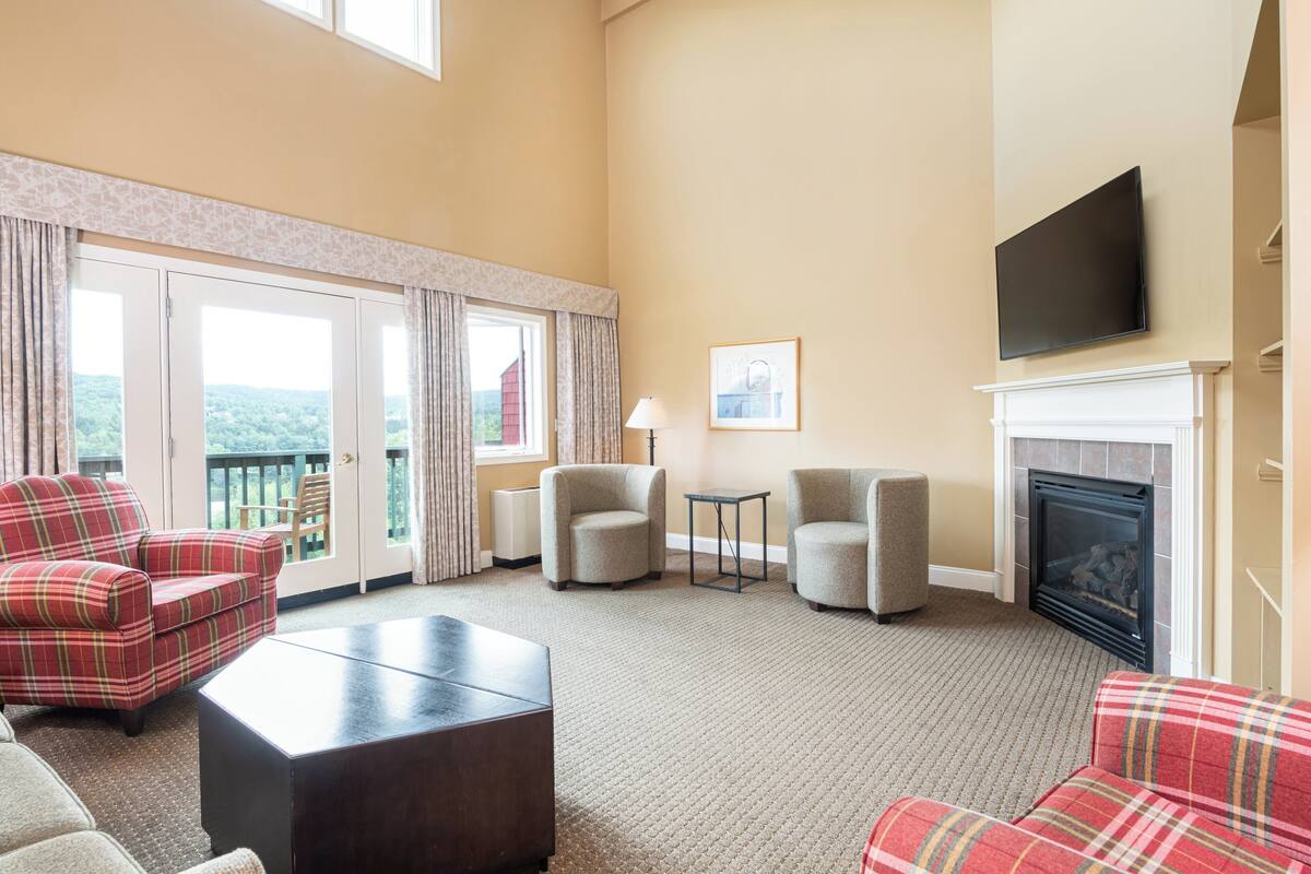 A spacious living room with a fireplace, a flat-screen TV, and a balcony with curtains.