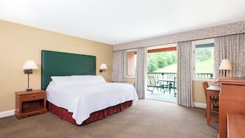 Habitación de hotel con una cama grande, dos mesitas de noche con lámparas, un aparador de madera y un balcón con vistas a zonas verdes.