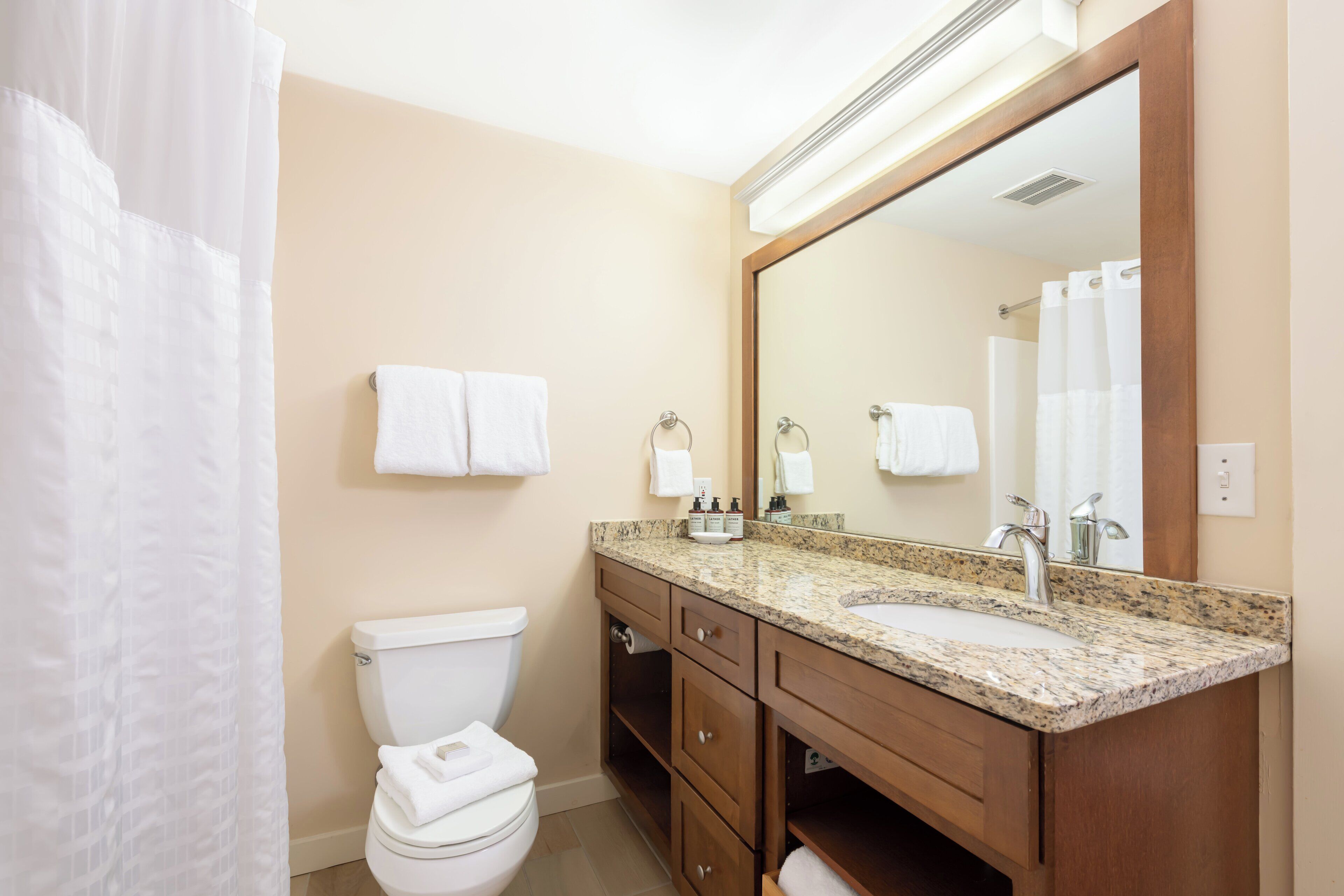 A bathroom with a toilet, sink, mirror, and towel racks.