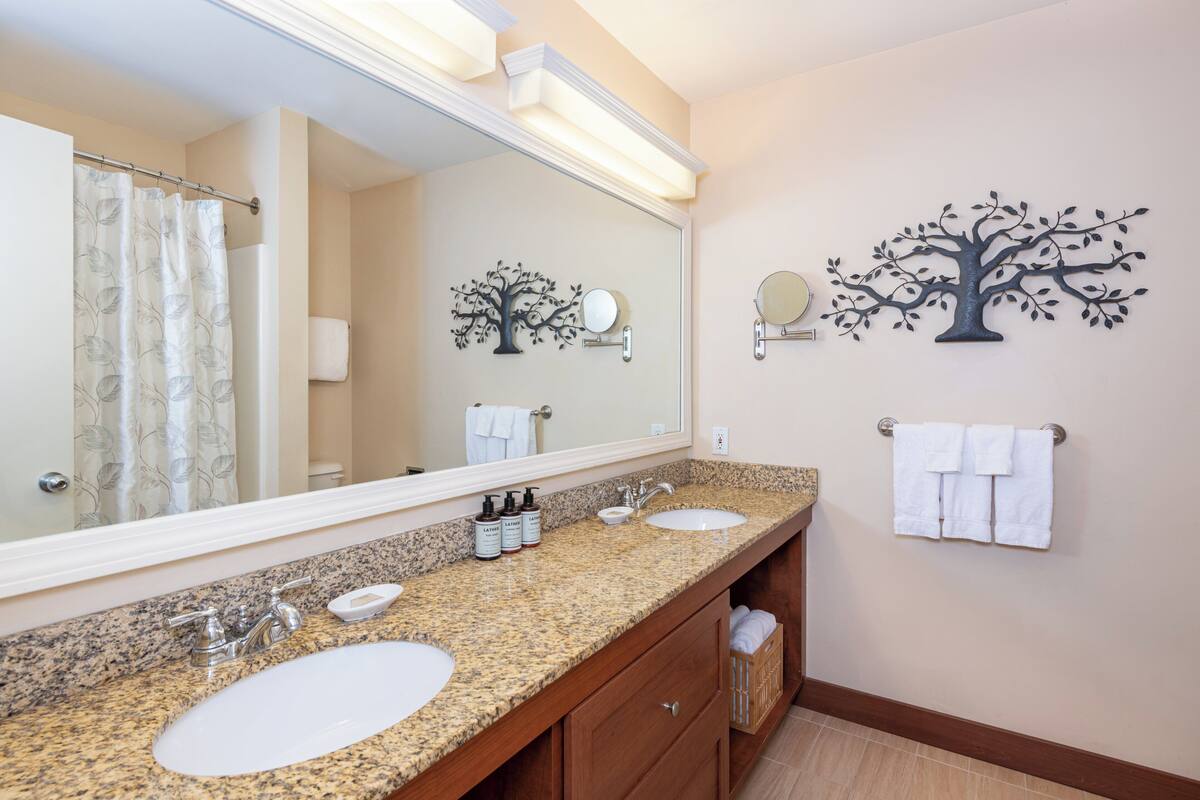 A bathroom with two sinks, a large mirror, and a tree-shaped wall decoration.