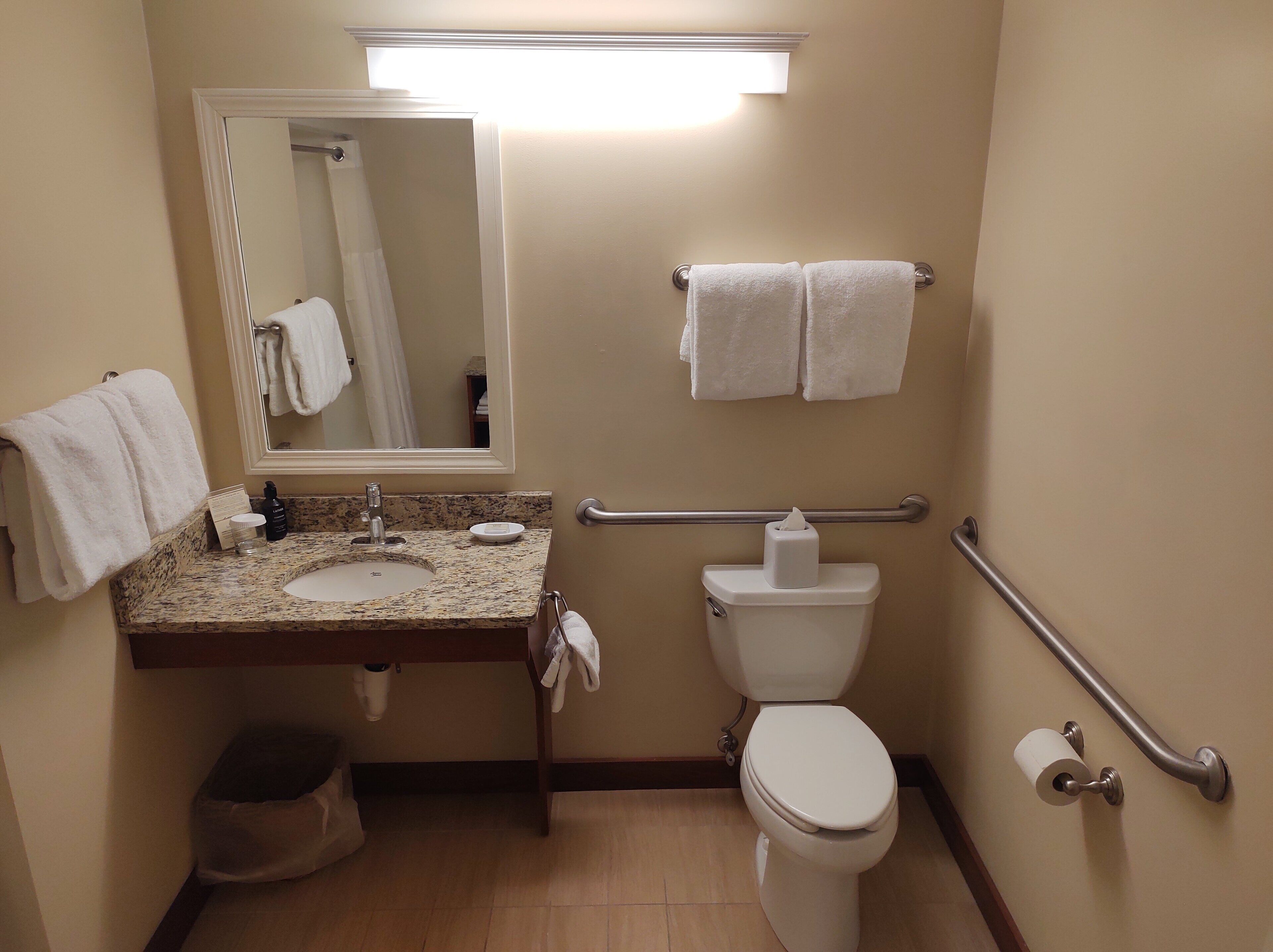 Ein kleines Badezimmer mit Waschbecken, Spiegel, Toilette und Haltegriffen.