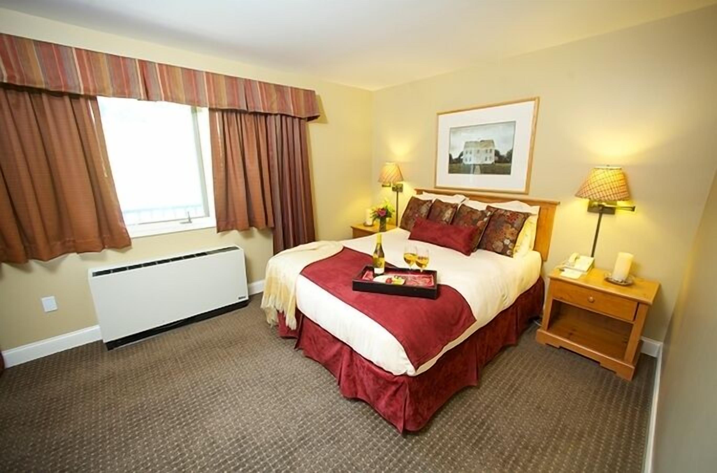 A hotel room with a large bed, two bedside tables, a window with curtains, a radiator, and a framed picture on the wall.