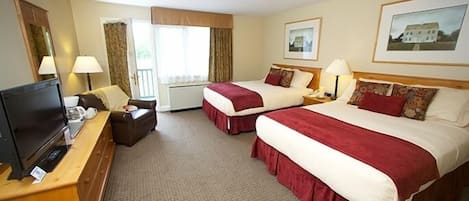 Quarto de hotel com duas camas, televisão, escrivaninha e janela com cortinas.