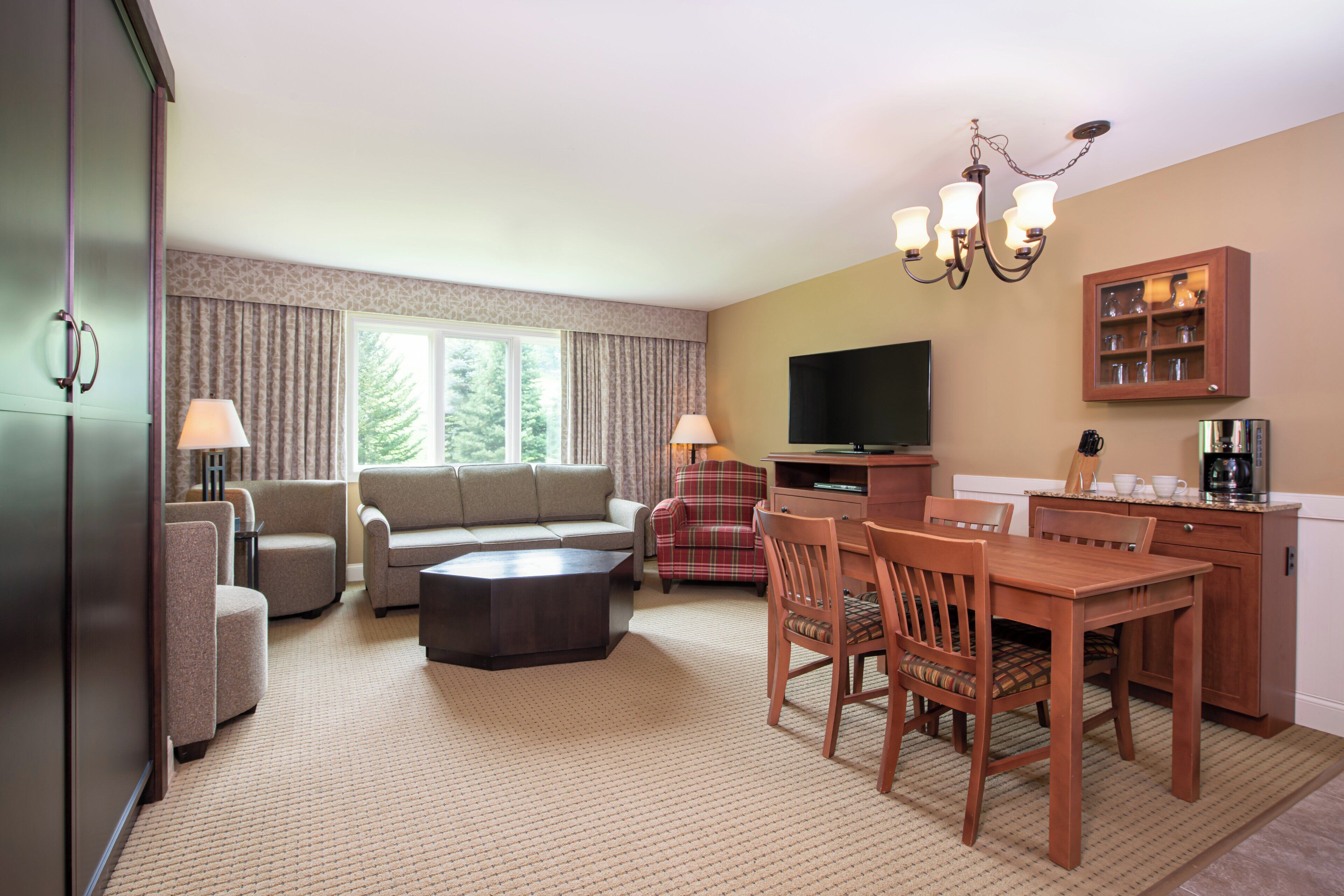 A hotel room with a living area, dining table, and a television.