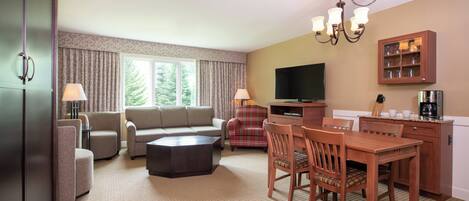 A hotel room with a living area, dining table, and a television.