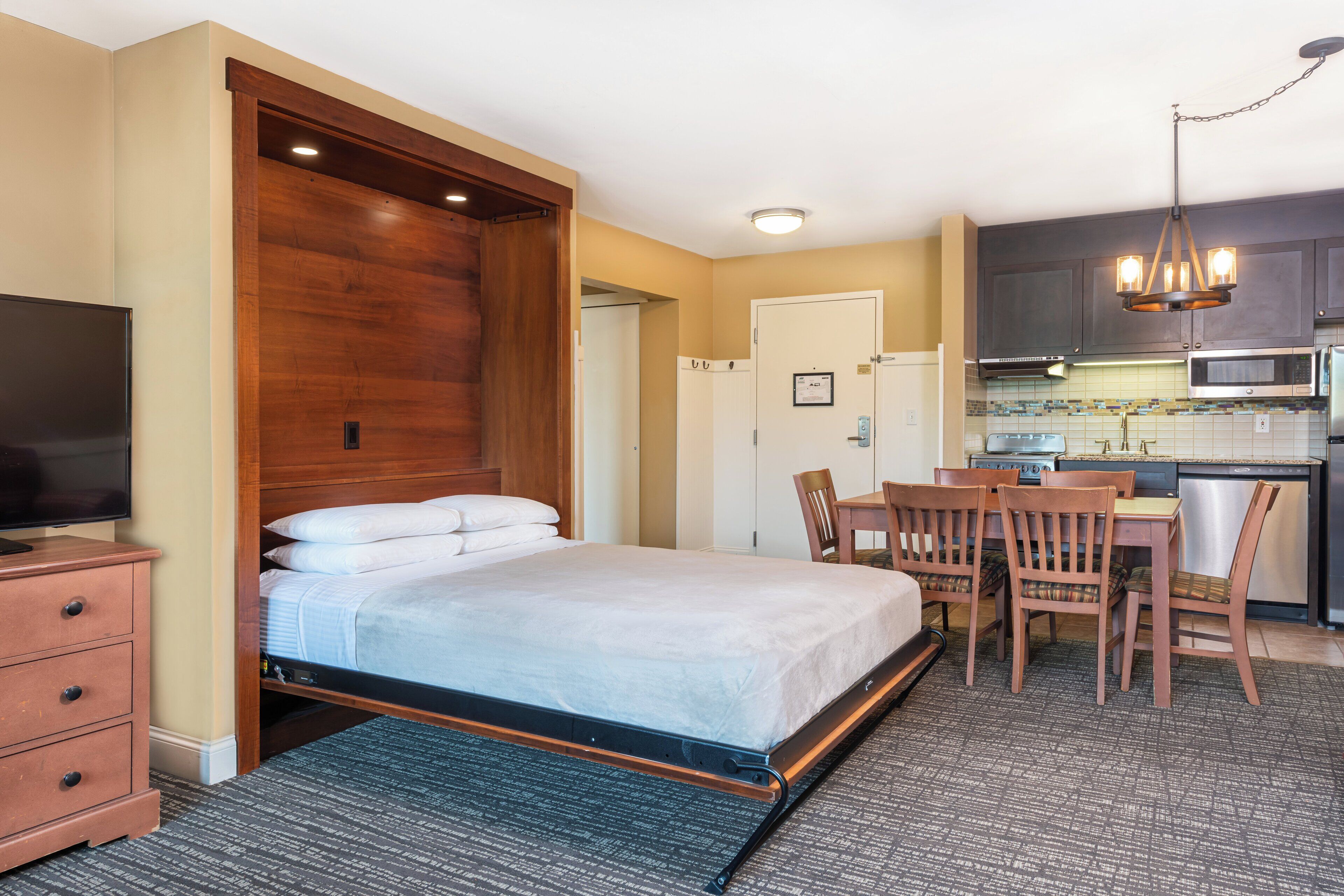 A hotel room with a bed, a desk, a chair, a television, and a kitchenette.