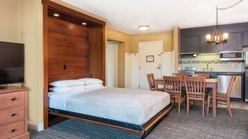 A hotel room with a bed, a desk, a chair, a television, and a kitchenette.