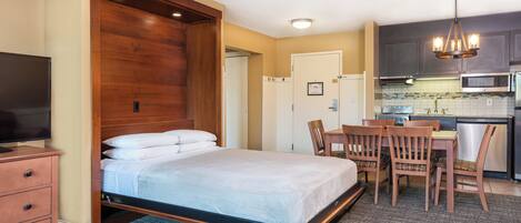 A hotel room with a bed, a desk, a chair, a television, and a kitchenette.