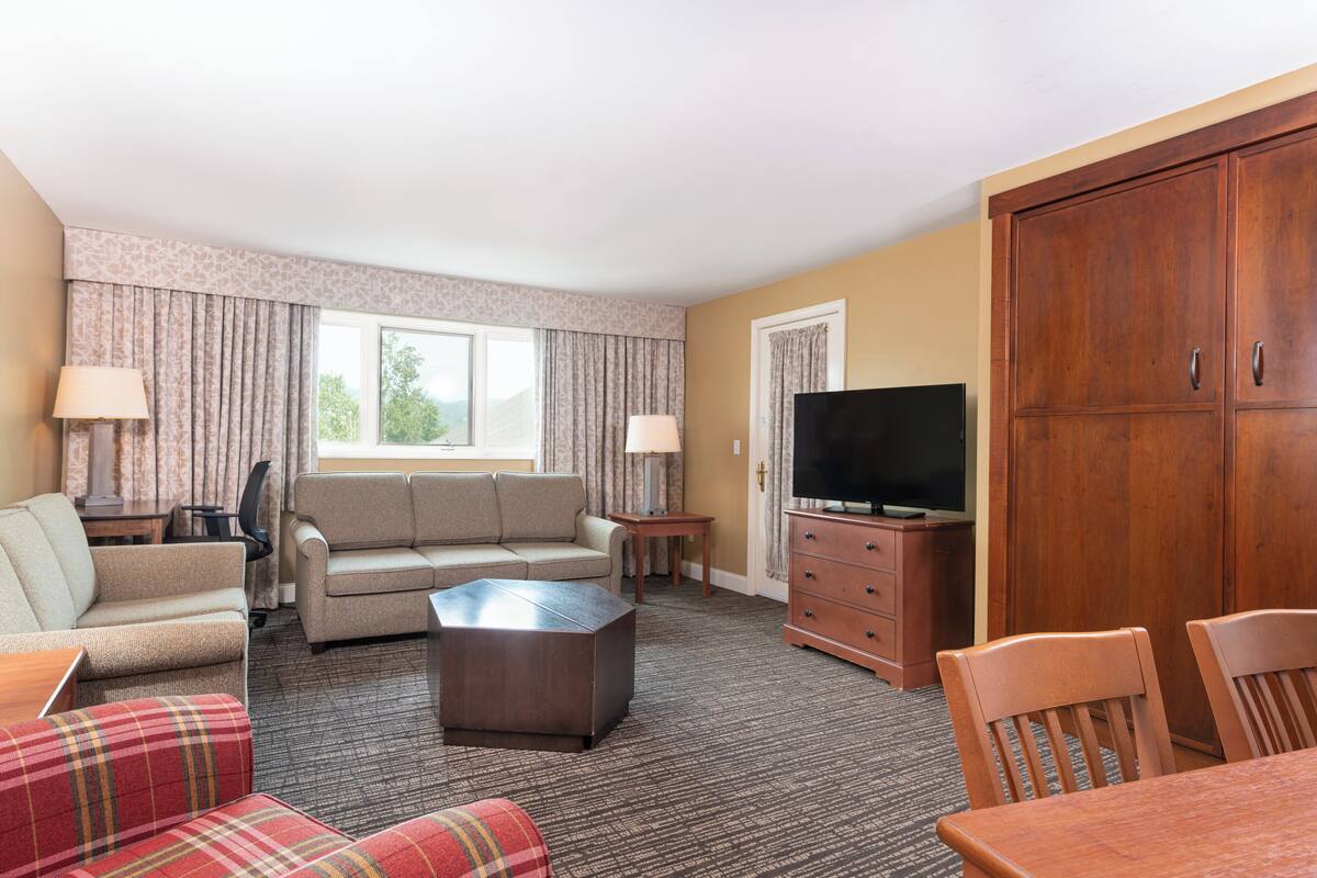 A hotel room with a sofa, a red plaid couch, a wooden coffee table, a TV, and a wardrobe.