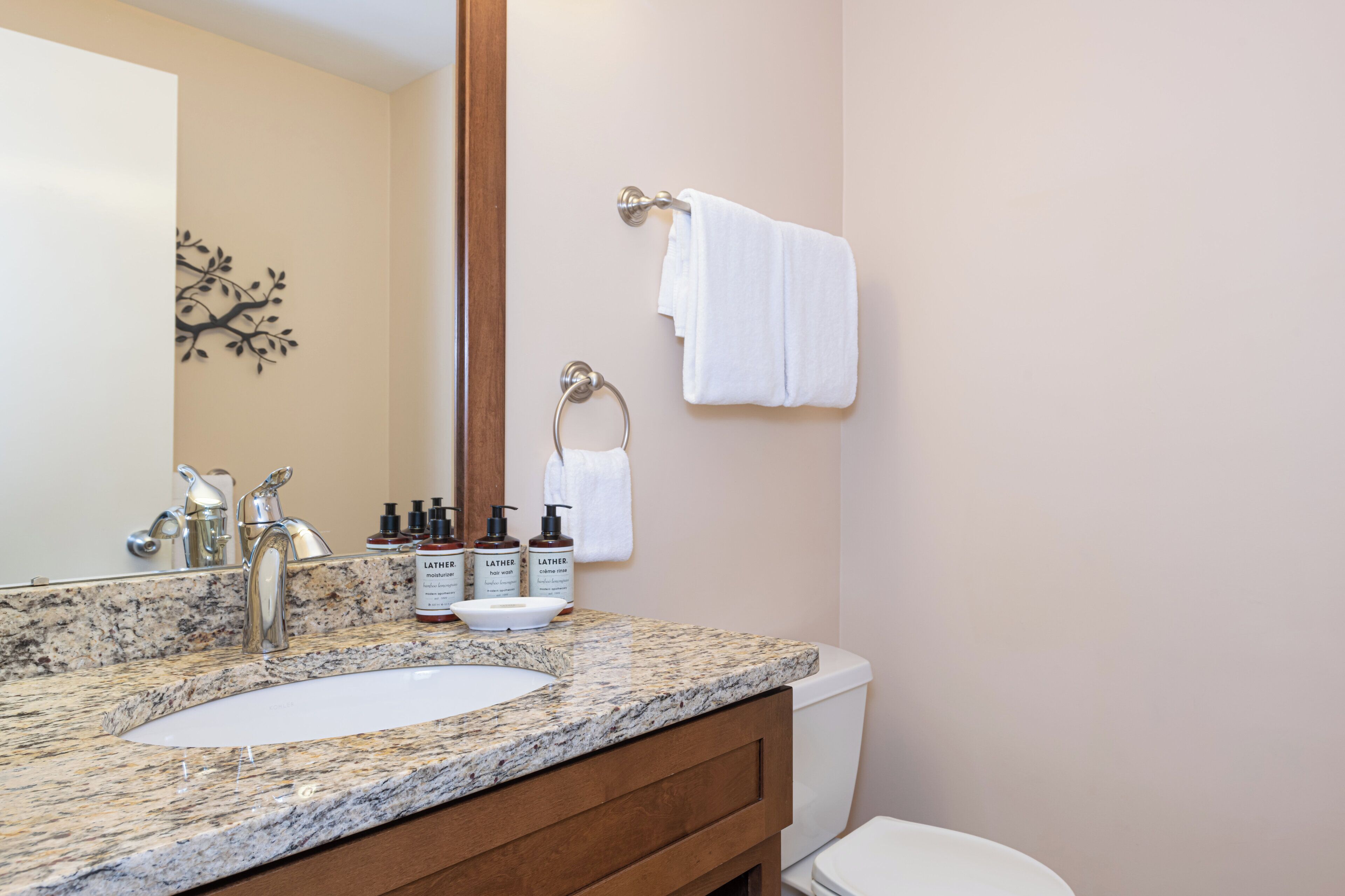 A bathroom with a granite countertop, a white sink, a mirror, a towel rack, and toiletries.