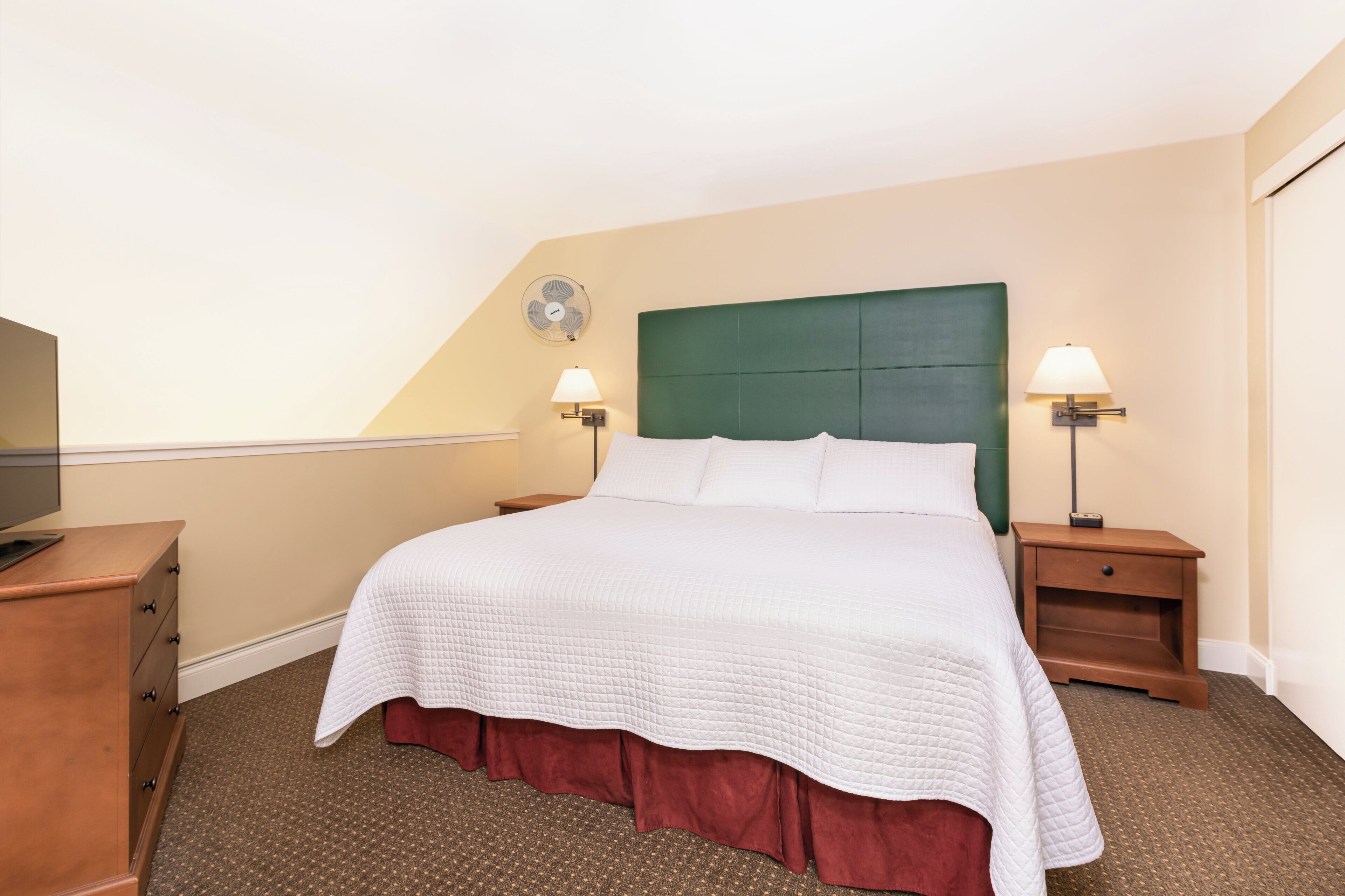 Ein Hotelzimmer mit einem großen Bett, zwei Nachttischen mit Lampen, einer Holzkommode und einem Deckenventilator.
