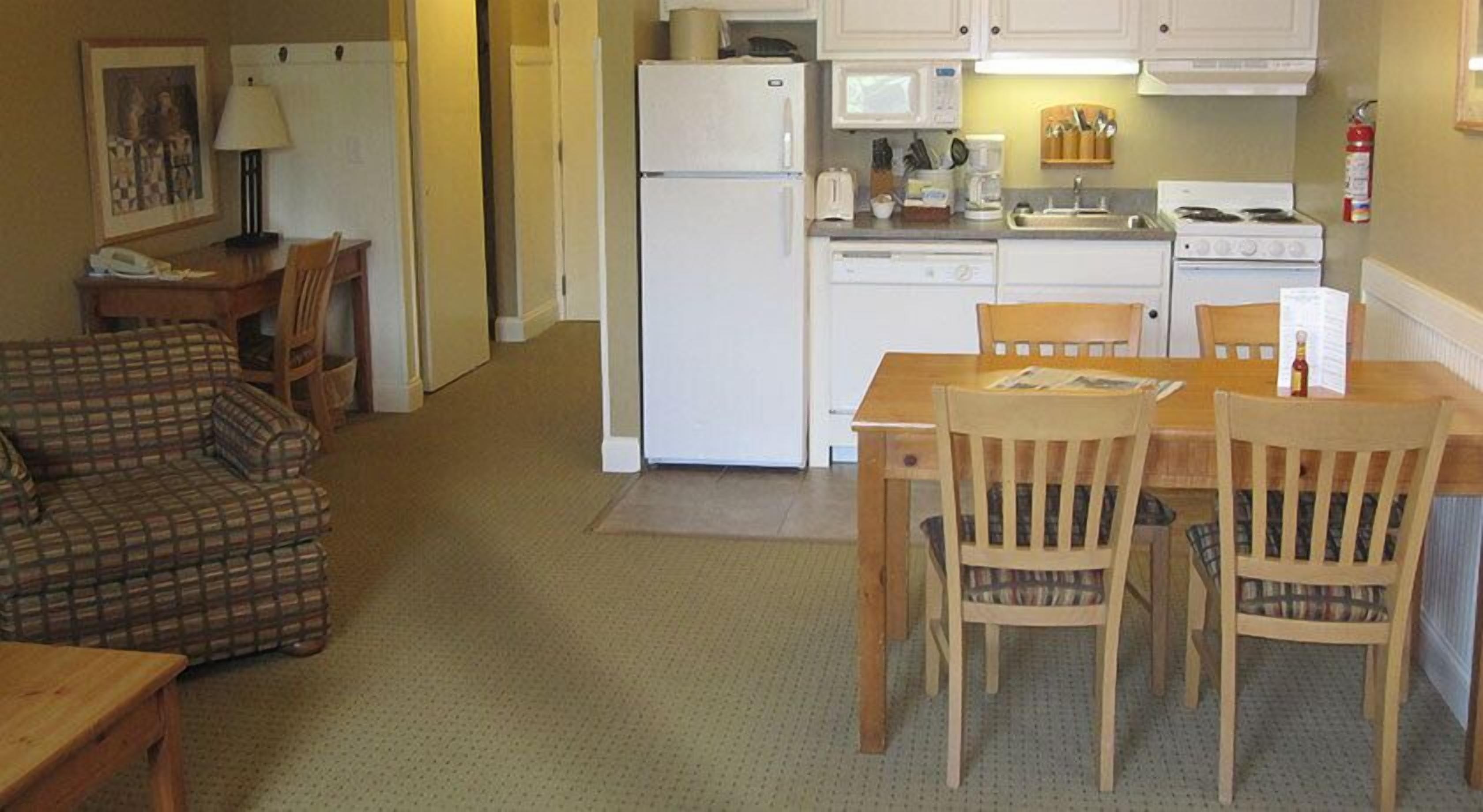 Un espacio habitable compacto con kitchenette, un comedor con sillas de madera, un sofá y una pequeña mesa.