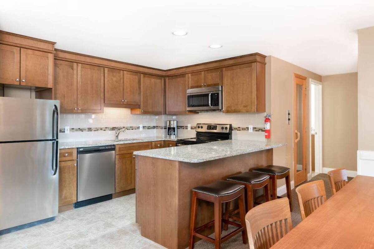 A modern kitchen with wooden cabinets, stainless steel appliances, a granite countertop, and a bar stool seating area.