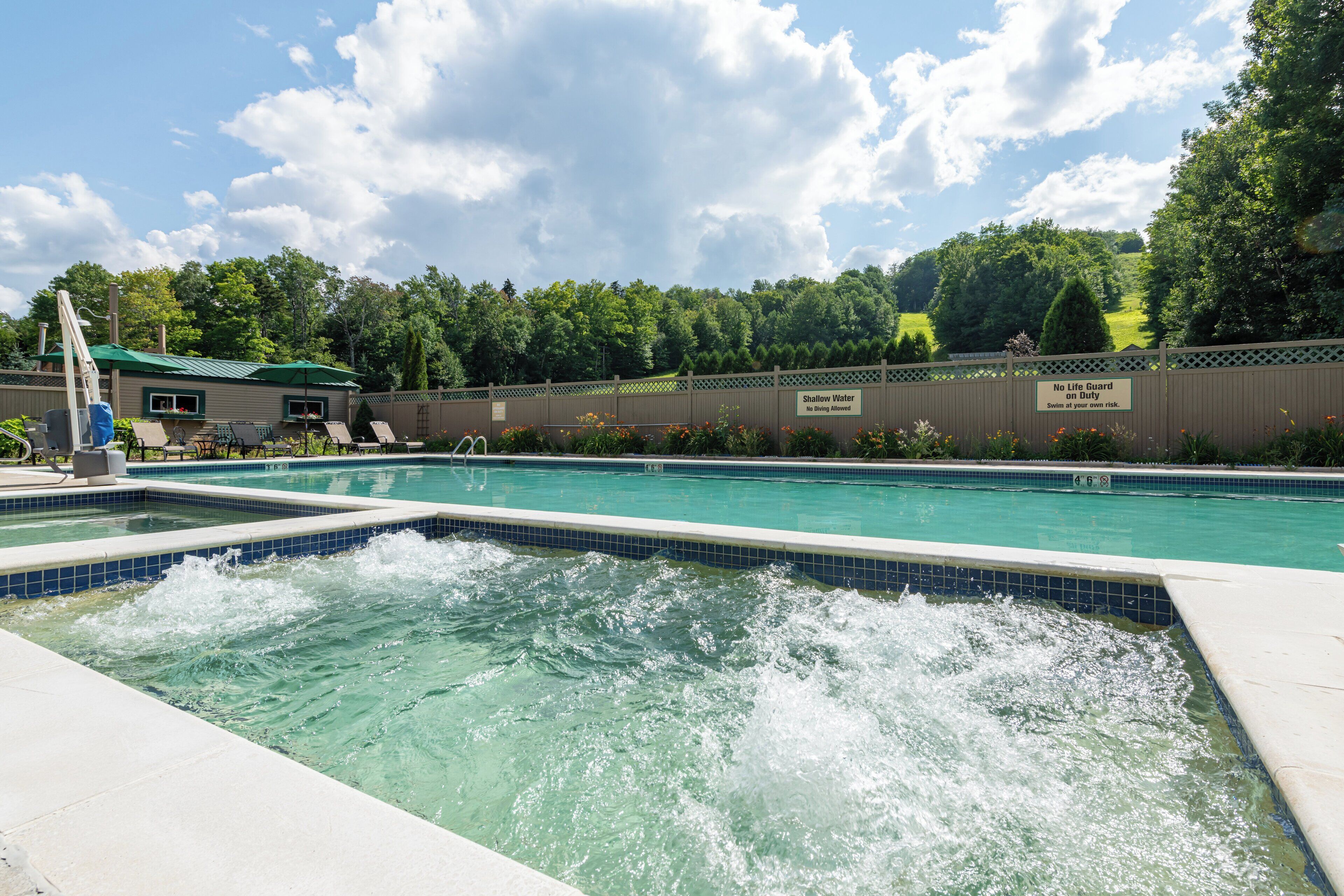A swimming pool with a water feature, surrounded by a fence and trees.