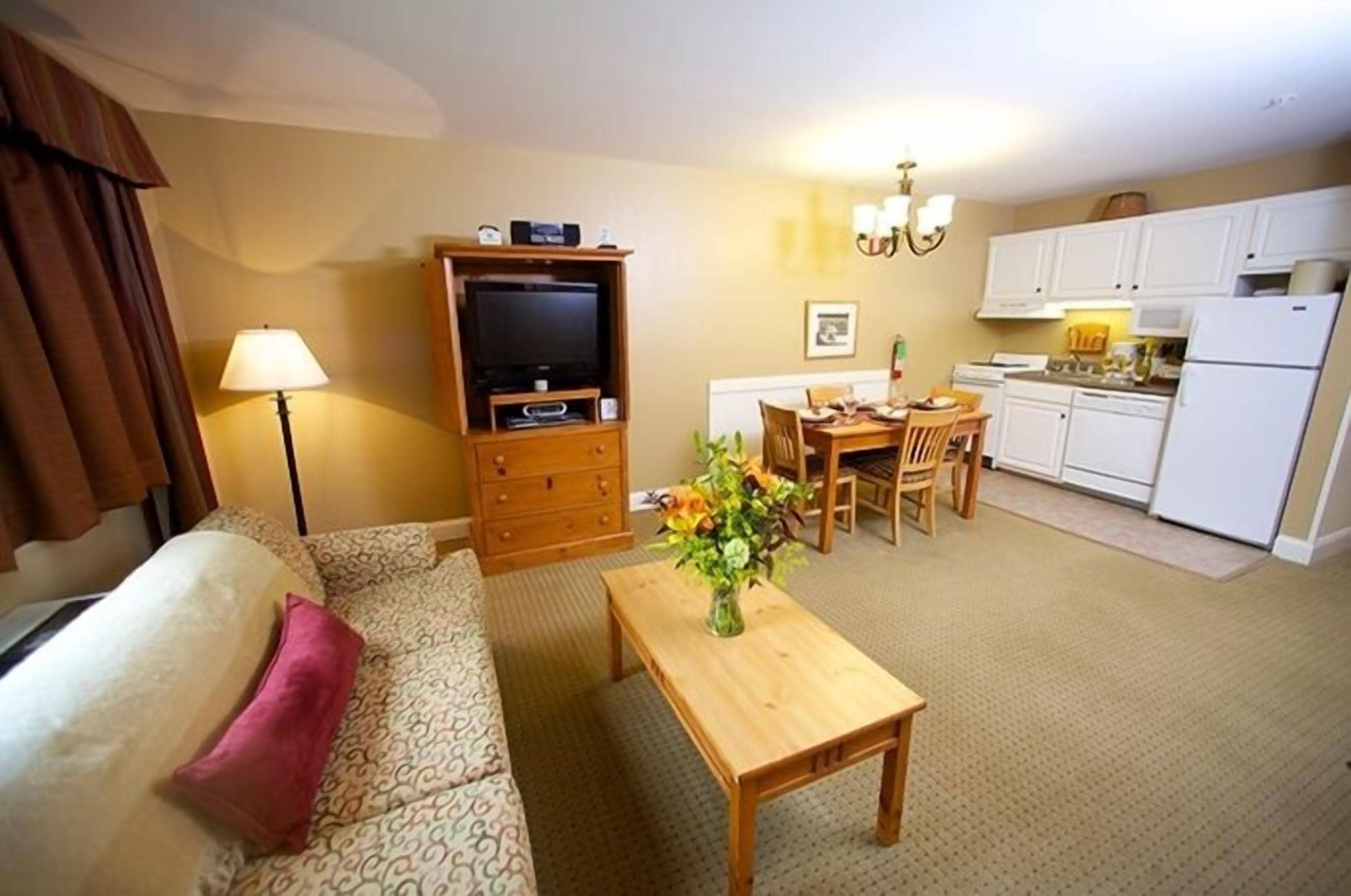 Un espacio habitable compacto con sofá, mesa de centro de madera, televisor, zona de comedor y kitchenette.