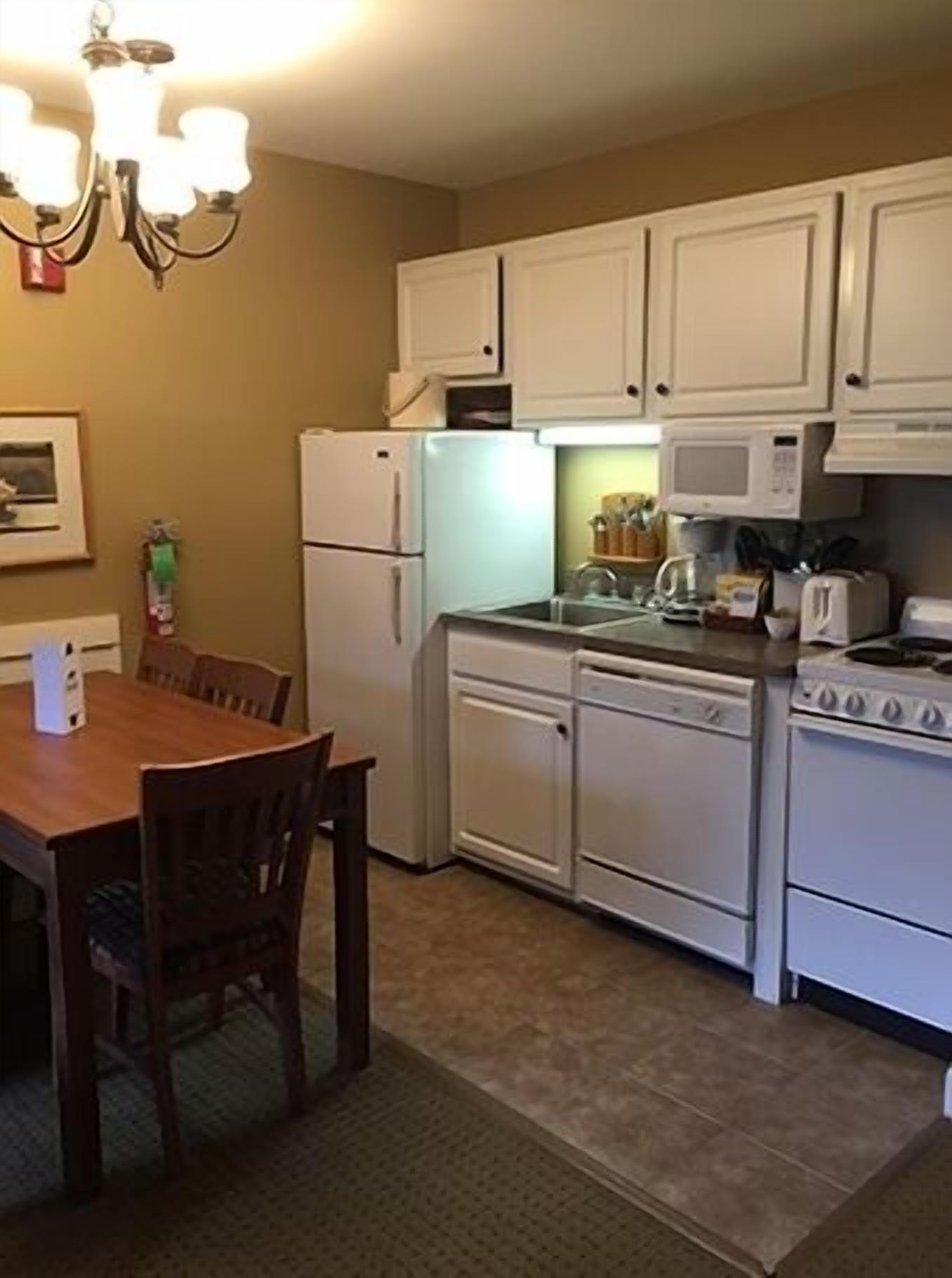 Une cuisine avec des meubles blancs, une cuisinière, un four à micro-ondes et une table à manger avec des chaises.