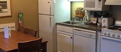 Une cuisine avec des meubles blancs, une cuisinière, un four à micro-ondes et une table à manger avec des chaises.