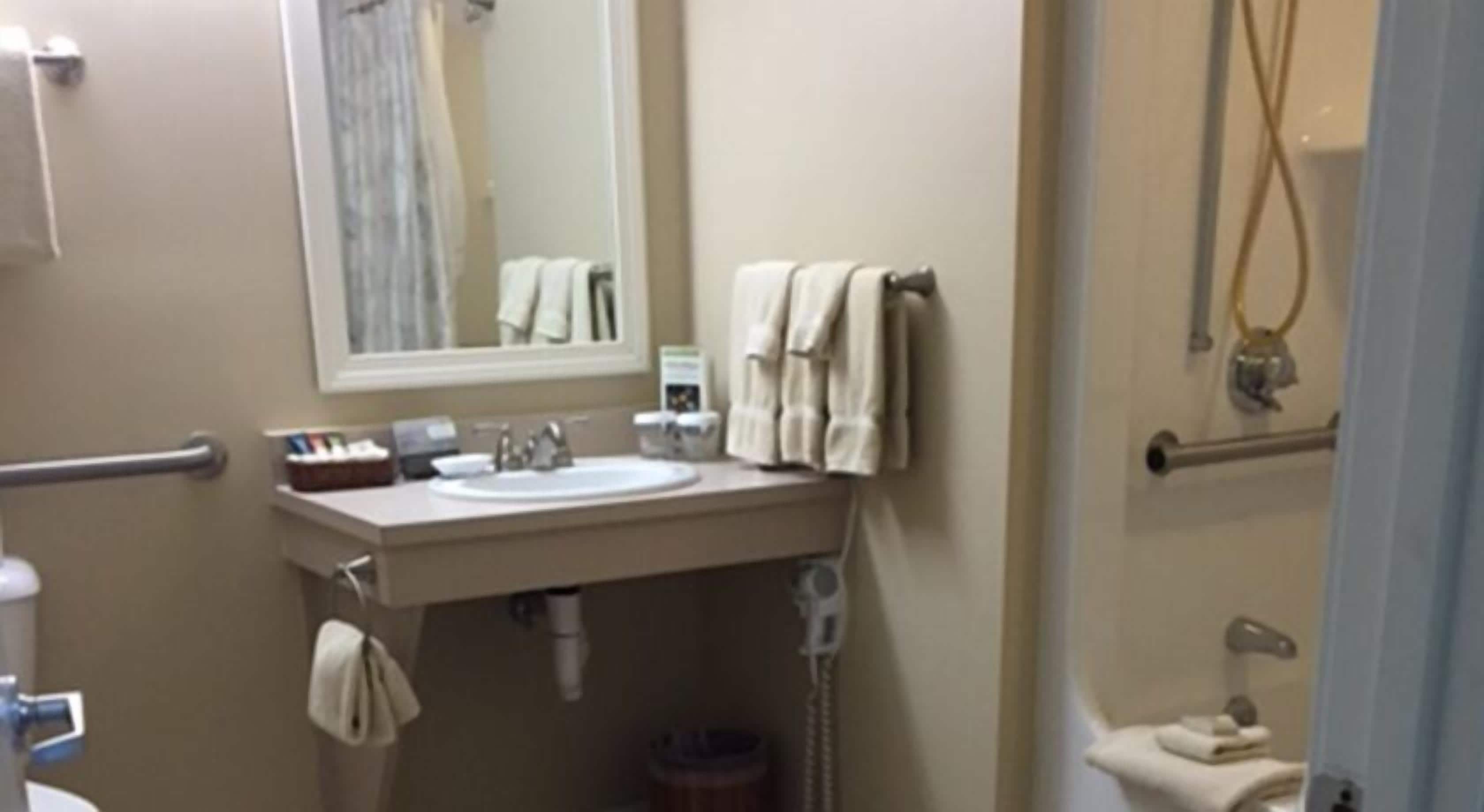 A bathroom with a sink, mirror, towel rack, and shower area.
