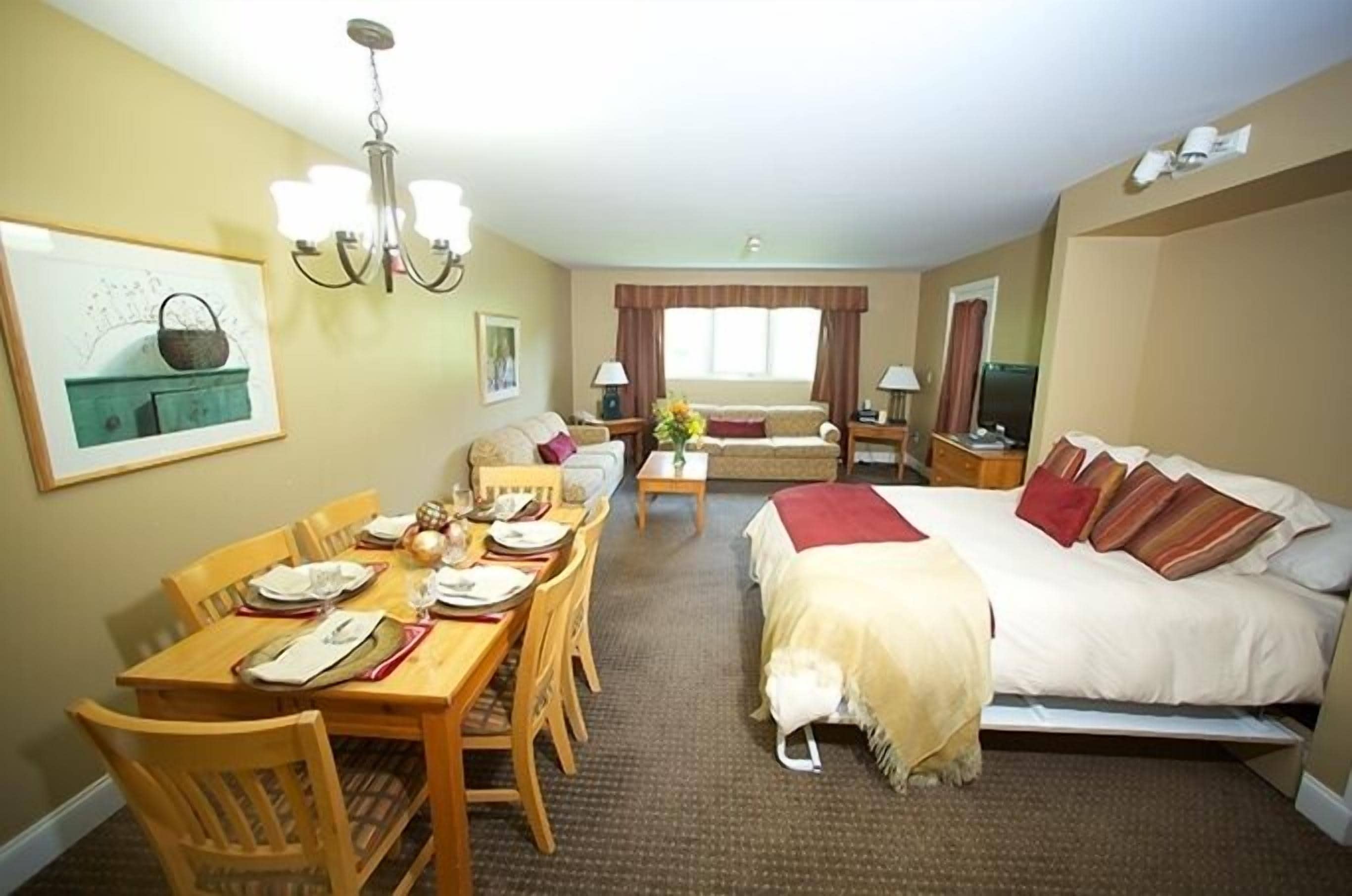 Una habitación de hotel con una cama, una mesa de comedor para dos personas, un sofá y un televisor.
