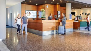 Un área de recepción de hotel moderna con un mostrador de madera, una pantalla digital mostrando un mensaje de bienvenida y una máquina de café.