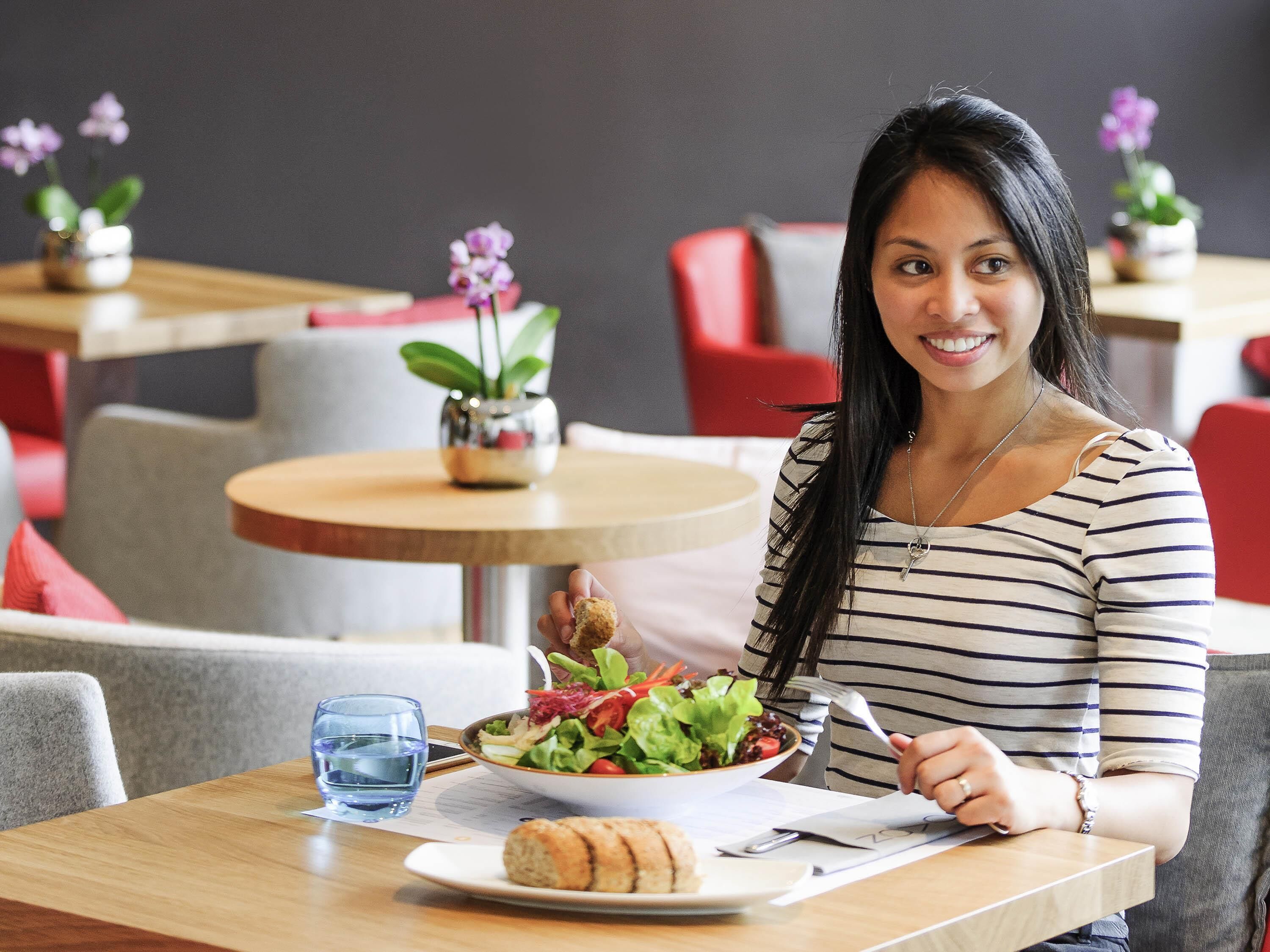 Une personne est assise à une table devant une assiette de nourriture, un verre d’eau et une serviette.