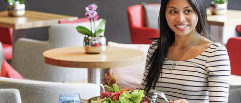 Une personne est assise à une table devant une assiette de nourriture, un verre d’eau et une serviette.