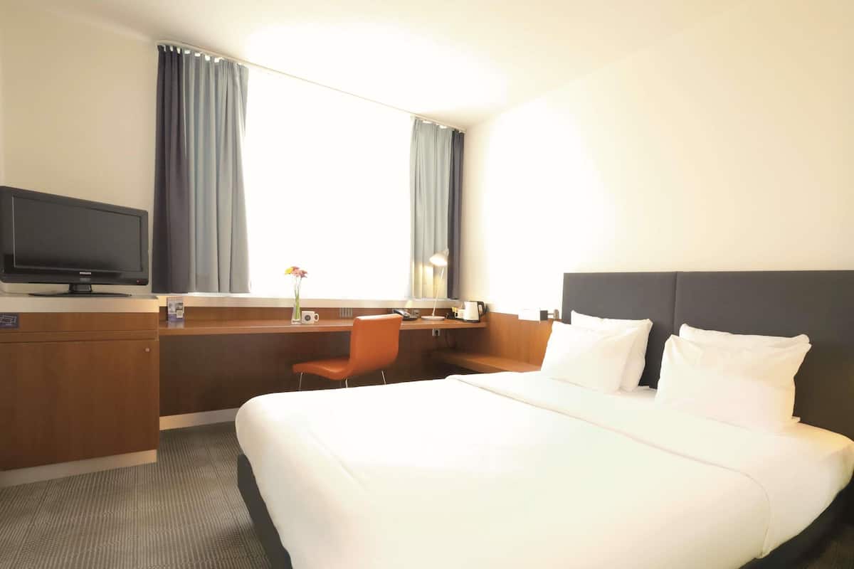 A hotel room with a large bed, a desk with a chair, a television, and a window with curtains.