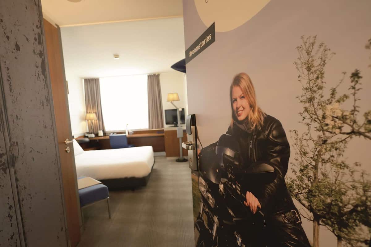 A hotel room with a bed, desk, chair, lamp, and a wall-mounted TV.