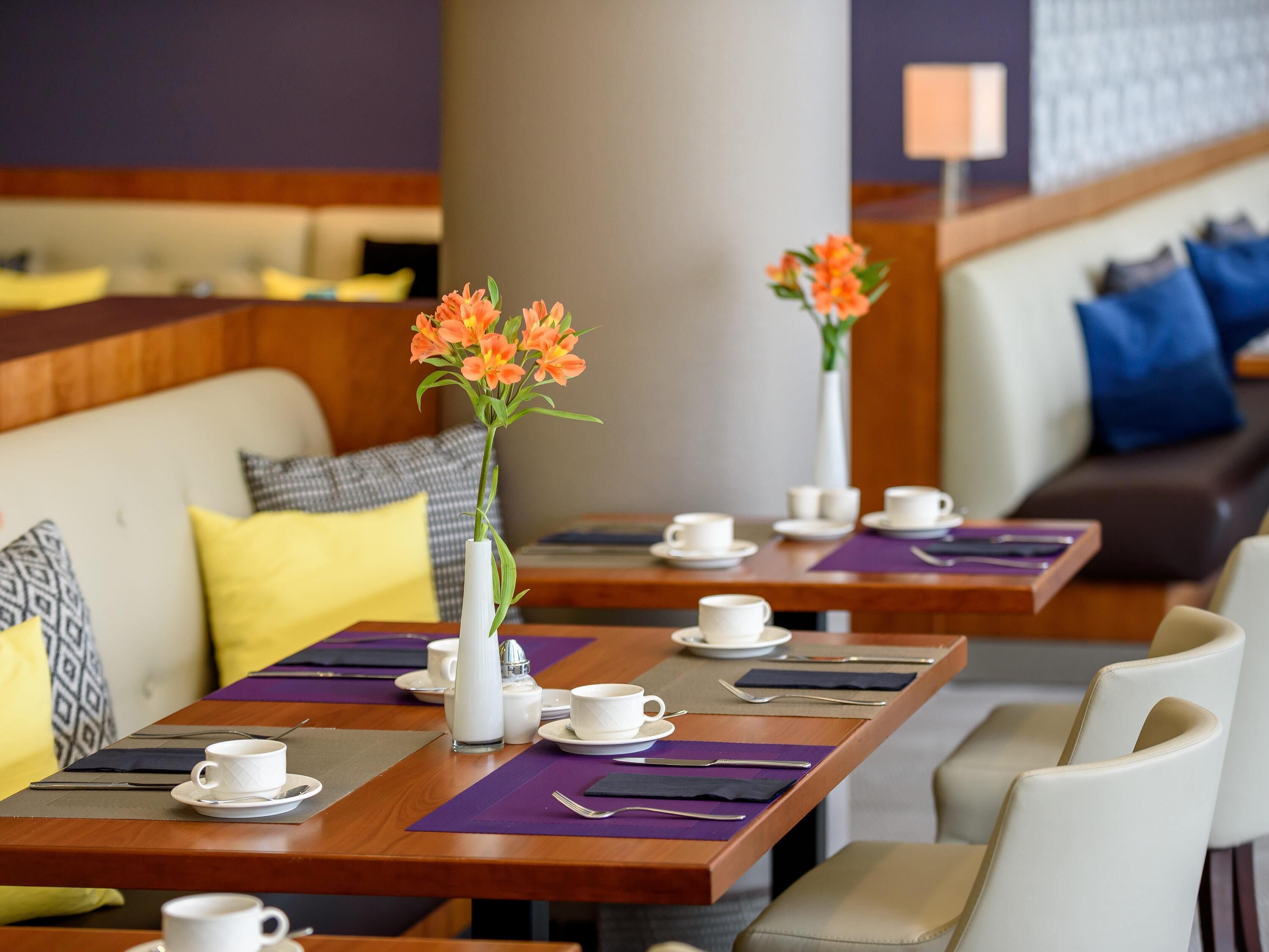 Un comedor de hotel con mesas dispuestas para comer, un sofá con cojines y un jarrón con flores.