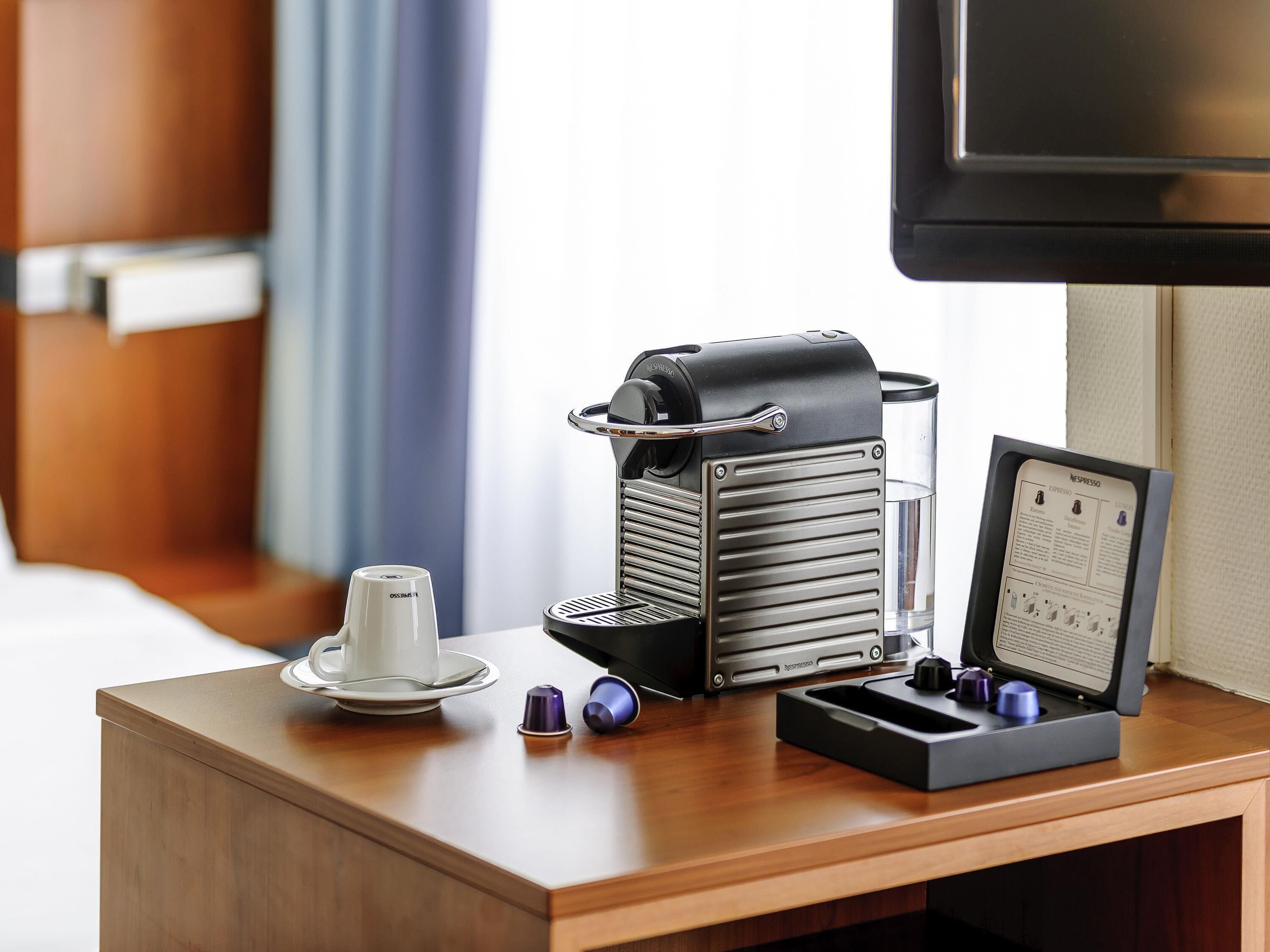 Une machine à café, une tasse et un menu sur une table en bois, dans une chambre d’hôtel.