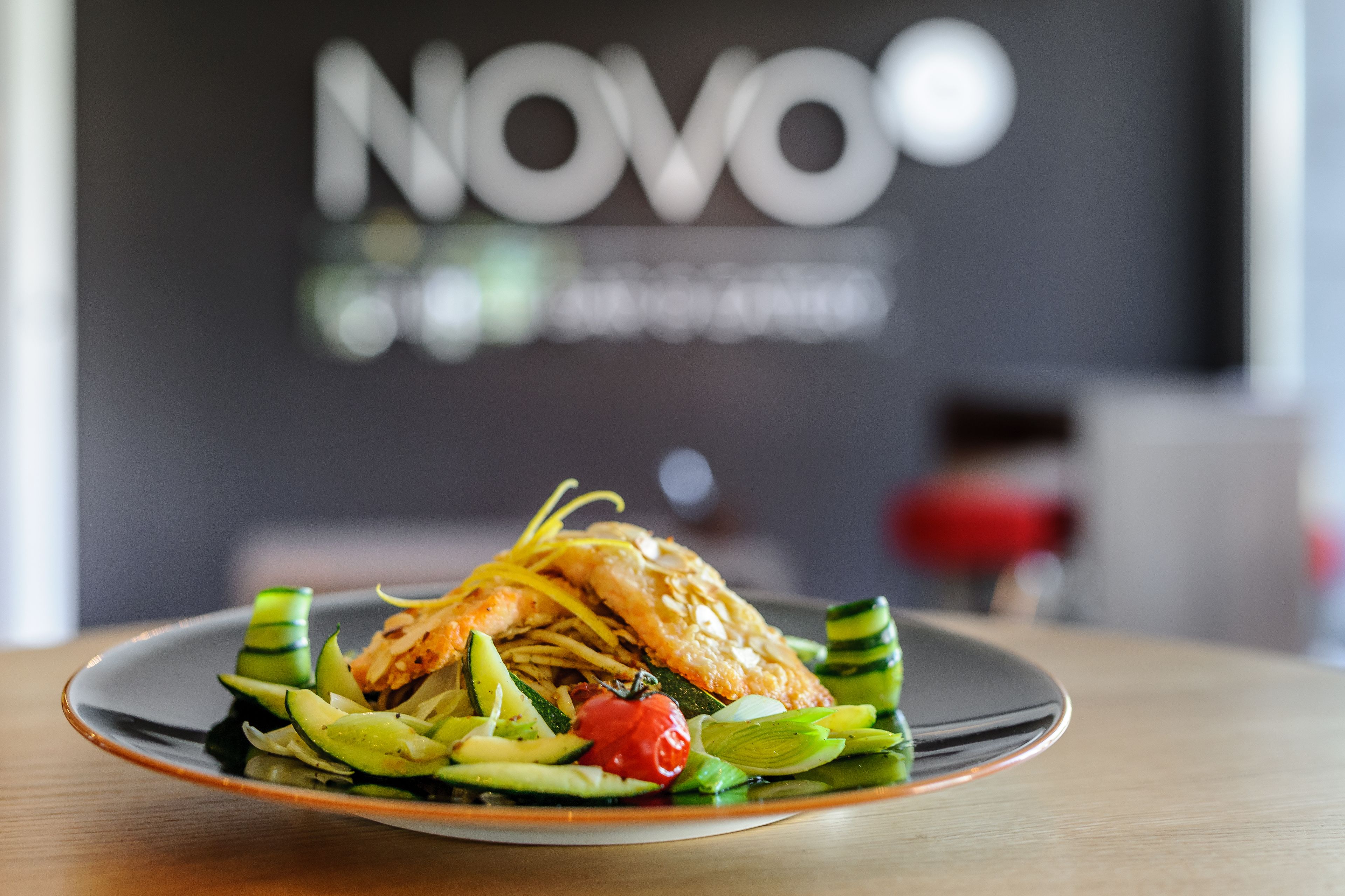 Un plato de comida sobre una mesa, con un fondo desenfocado que muestra un letrero con el texto "NOVO".