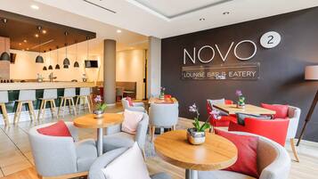 Eine moderne Lounge-Bar und ein Restaurant mit grauen und roten Sitzgelegenheiten, Holztischen und Pendelleuchten.