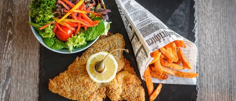 Un plato con filetes de pescado empanizado, una ensalada y patatas fritas sobre una tabla de pizarra.