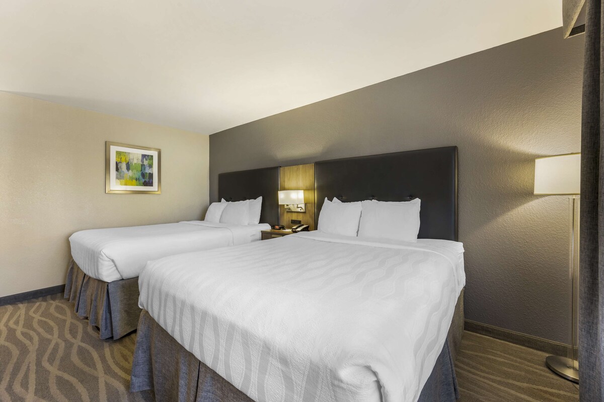 A hotel room with two beds, a nightstand, a lamp, and a framed picture on the wall.