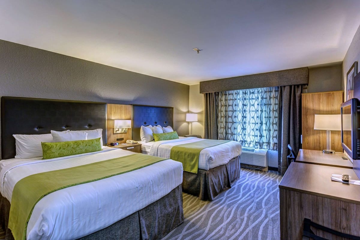 A hotel room with two beds, a desk, a TV, and a window with curtains.