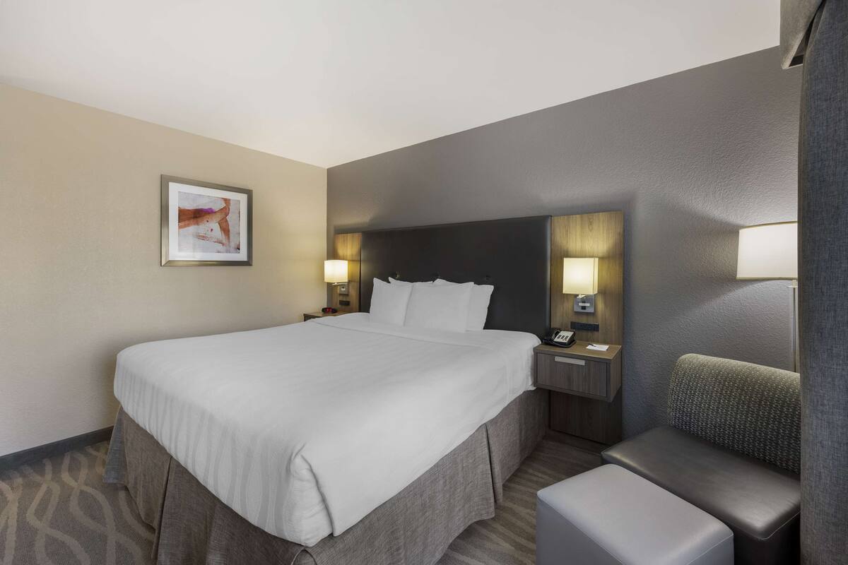 A hotel room with a large bed, bedside tables with lamps, a chair, and a framed picture on the wall.