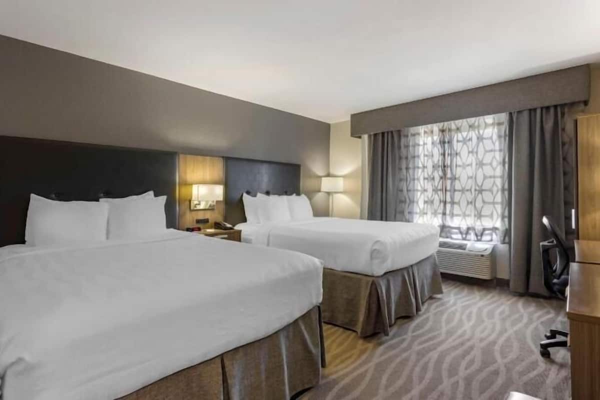 A hotel room with two beds, a desk, a chair, and a window with curtains.
