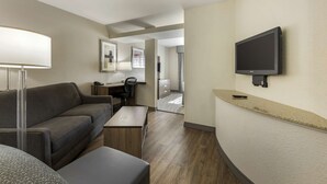Una habitación de hotel moderna con un sofá, un escritorio, un televisor de pantalla plana montado en la pared y una pequeña mesa.
