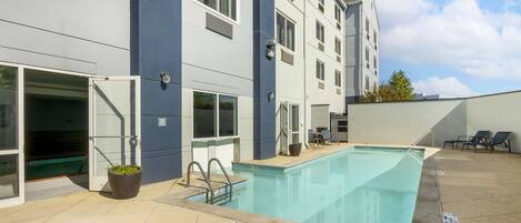 An outdoor swimming pool with a clear blue water surface, adjacent to a building with multiple windows and a door.