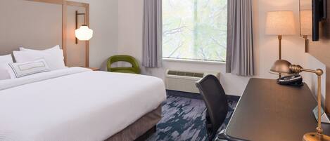Habitación de hotel con cama, escritorio, silla, lámpara, televisión y ventana con cortinas.