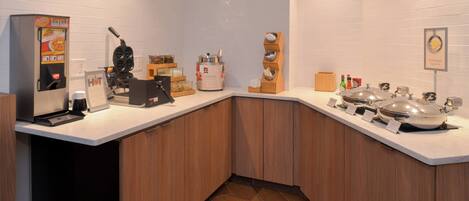 A modern kitchen with a built-in waffle maker, a coffee machine, and a variety of condiments and utensils on the counter.
