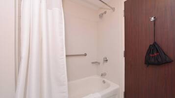 Une salle de bain avec une baignoire, une douche, un porte-serviettes et une porte sur laquelle est accroché un sac.