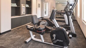 Ein Fitnessraum mit Trainingsgeräten, einer Uhr und Regalen.