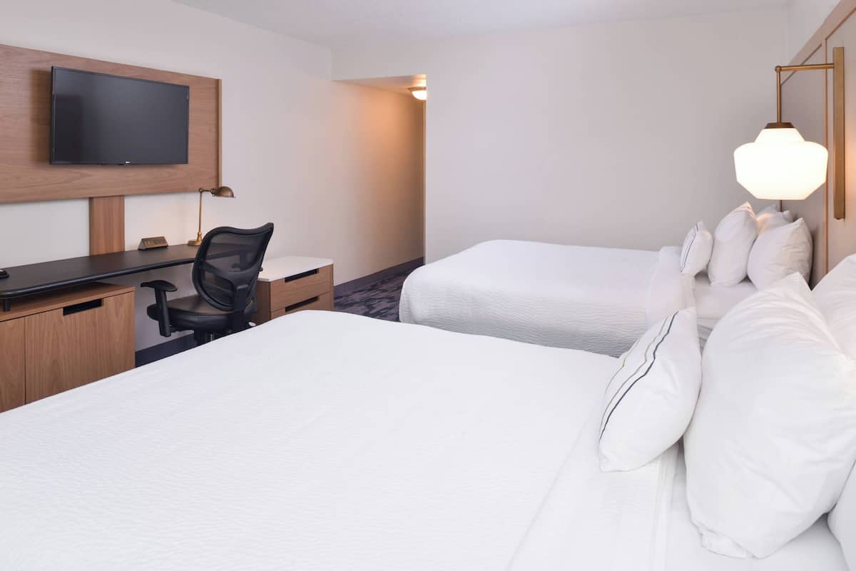 Une chambre d’hôtel avec deux lits, un bureau, une chaise, une télévision et une lampe.
