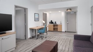 A modern hotel room with a flat-screen TV, a desk with a chair, a sofa, and a small kitchenette. - Hilton Garden Inn Rockaway (Rockaway)