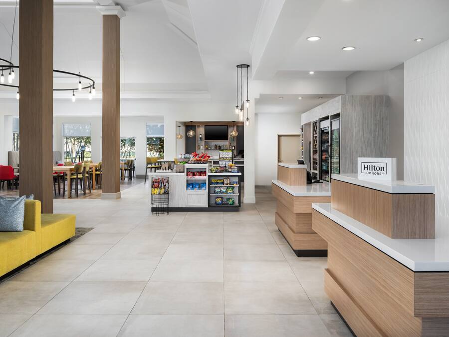 A modern hotel lobby with a reception desk, seating area, and a bar.