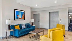 Un salon moderne avec un canapé bleu, un fauteuil jaune et une table basse. Un tableau encadré est accroché au mur, et une porte est visible au fond.